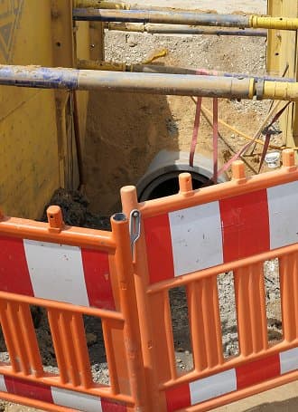 Baugrube mit Absperrung und Rohren für ein Kanalsystem auf einer Baustelle.