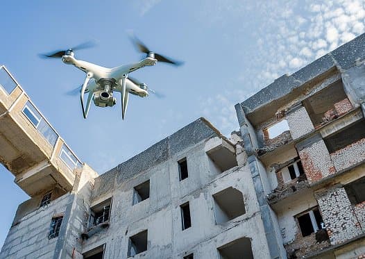 Drohne fliegt vor einem verlassenen, teilweise zerstörten Gebäude mit leeren Fensterrahmen.