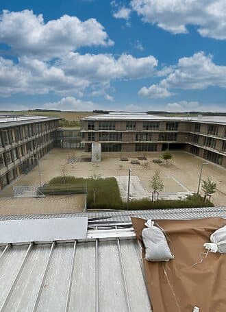 Blick auf den Innenhof eines modernen Gebäudekomplexes mit Flachdach und begrüntem Hof bei bewölktem Himmel.