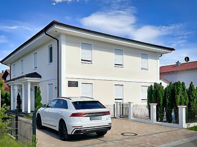 Modernes zweistöckiges Wohnhaus mit weißer Fassade und dunkelrotem Dach mit sachverständigenbüro und blauen Himmel im Hintergrund.