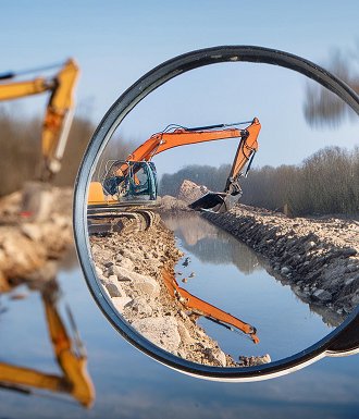 Bagger bei der Arbeit an einem Wasserkanal auf einer Baustelle, durch eine Lupe betrachtet.